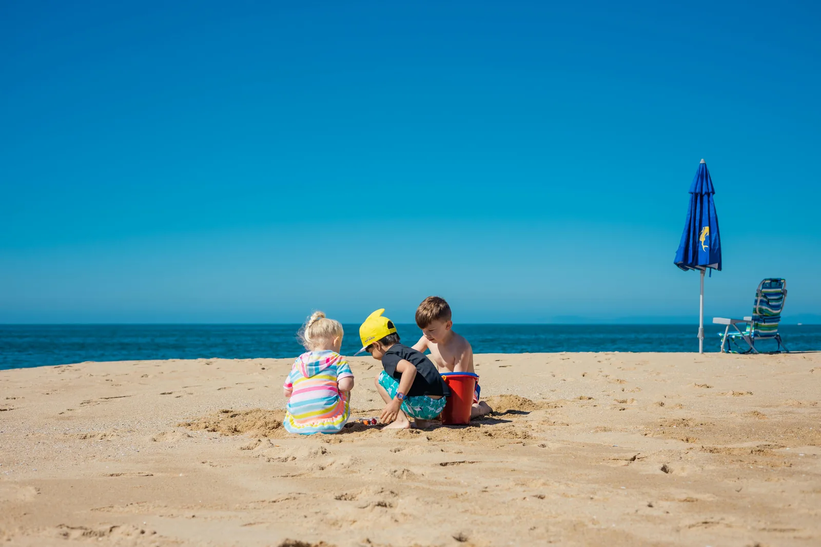 Plage familiale avec parasols et enfants qui jouent dans le sable.