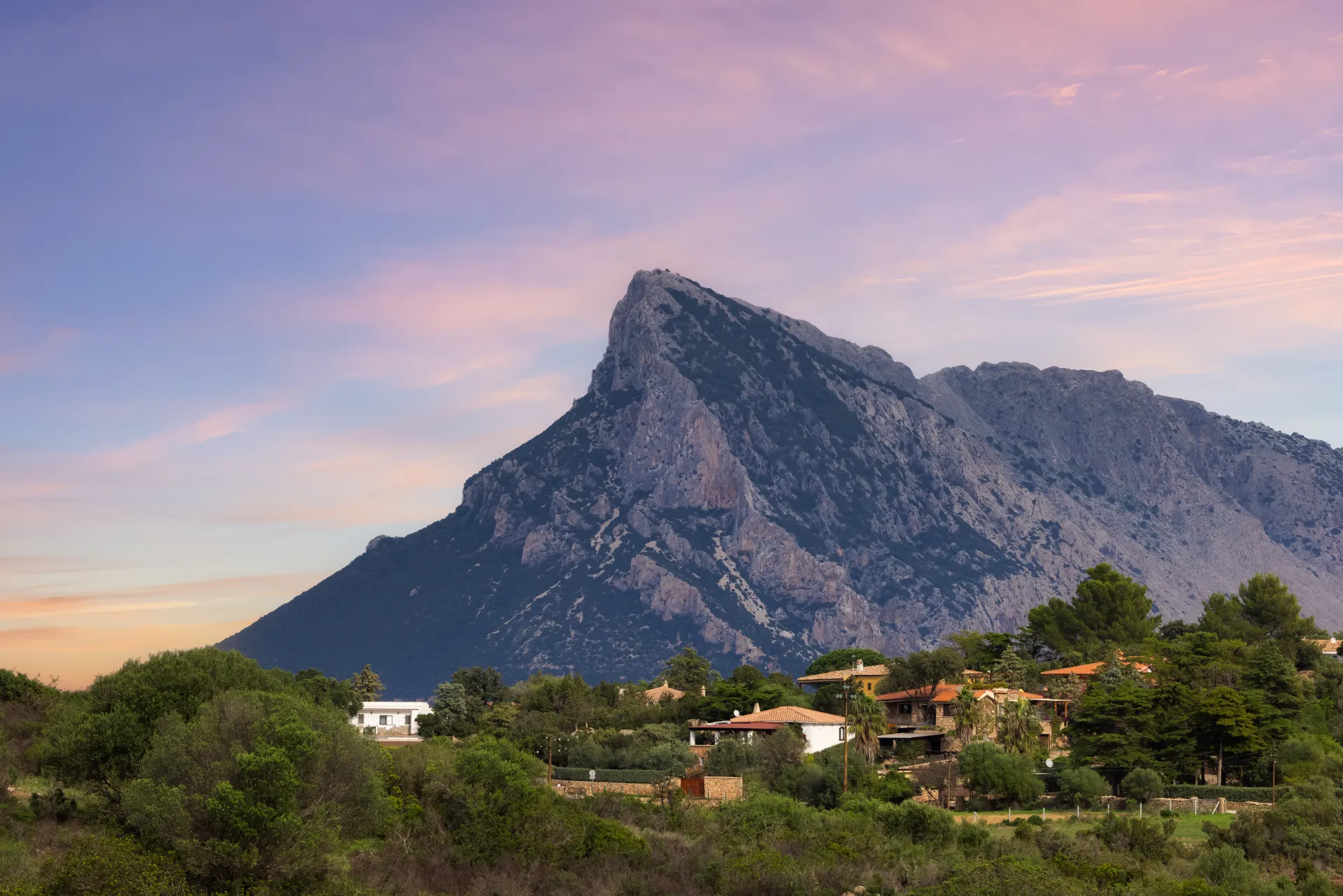 Paysage montagneux avec des maisons traditionnelles et une végétation méditerranéenne luxuriante sous un ciel pastel au lever ou coucher du soleil