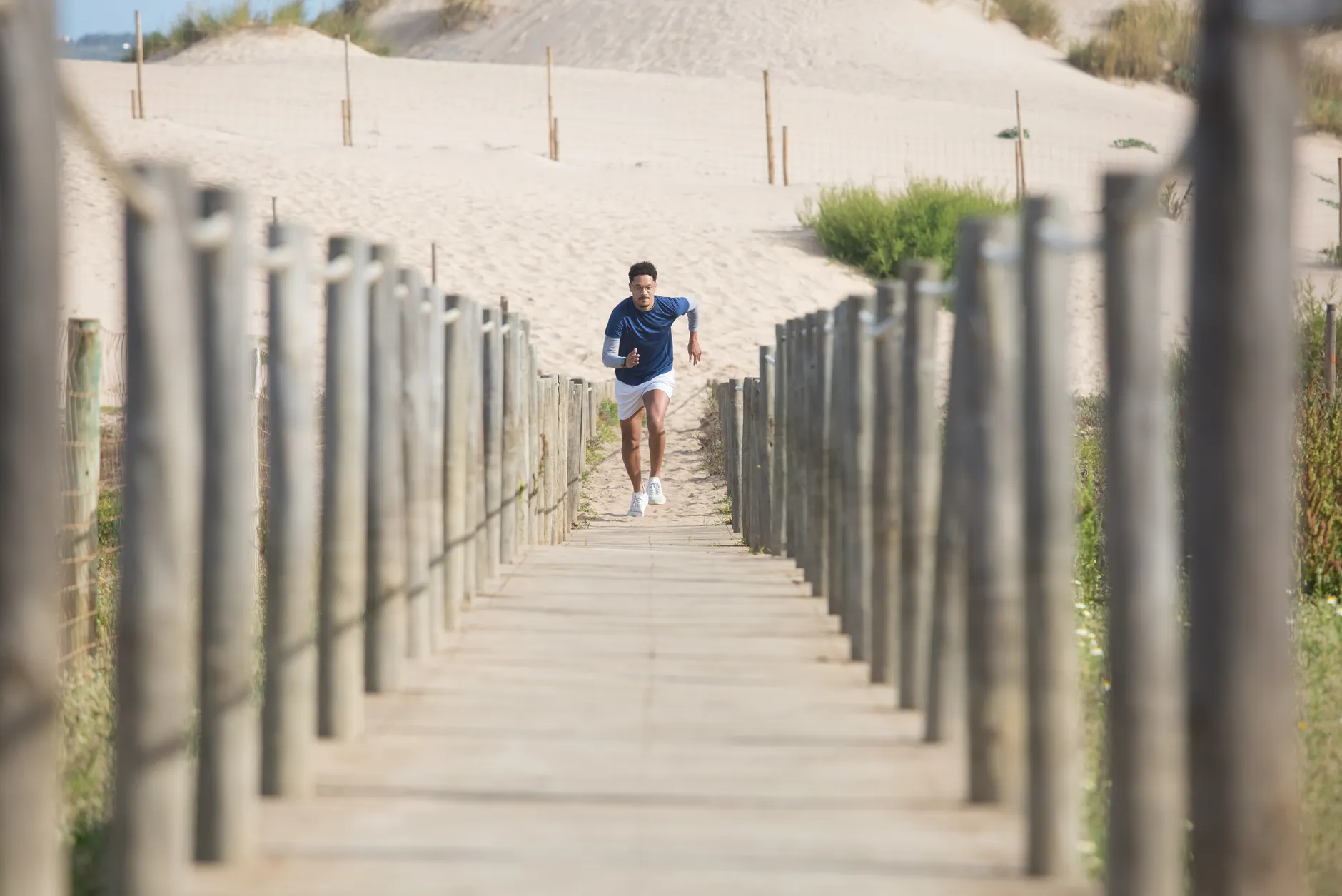 Man in activewear running on a wooden boardwalk at a scenic beach. Perfect for fitness and lifestyle themes.