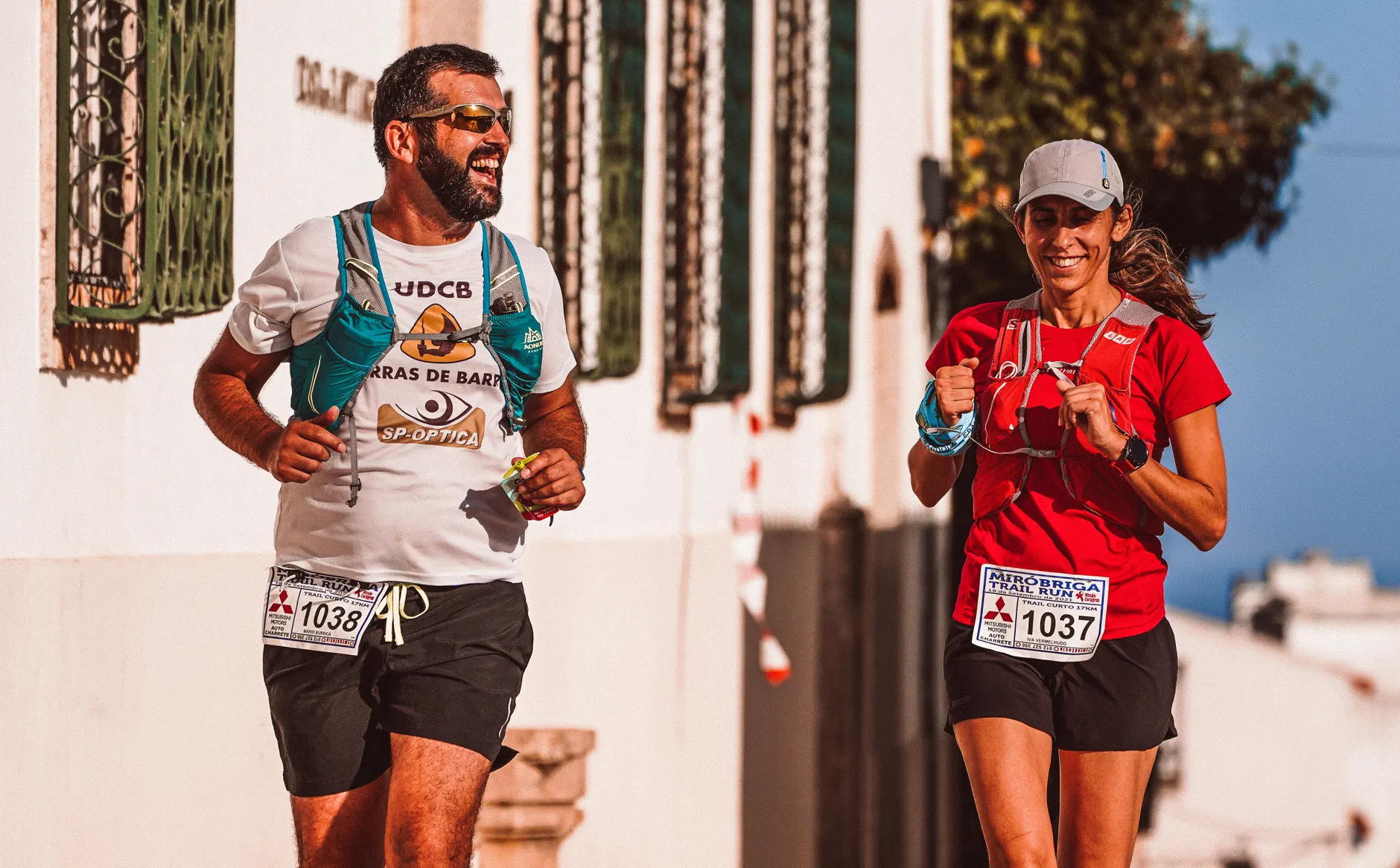 Two athletes joyfully running in an outdoor trail race, enjoying the sunny day.