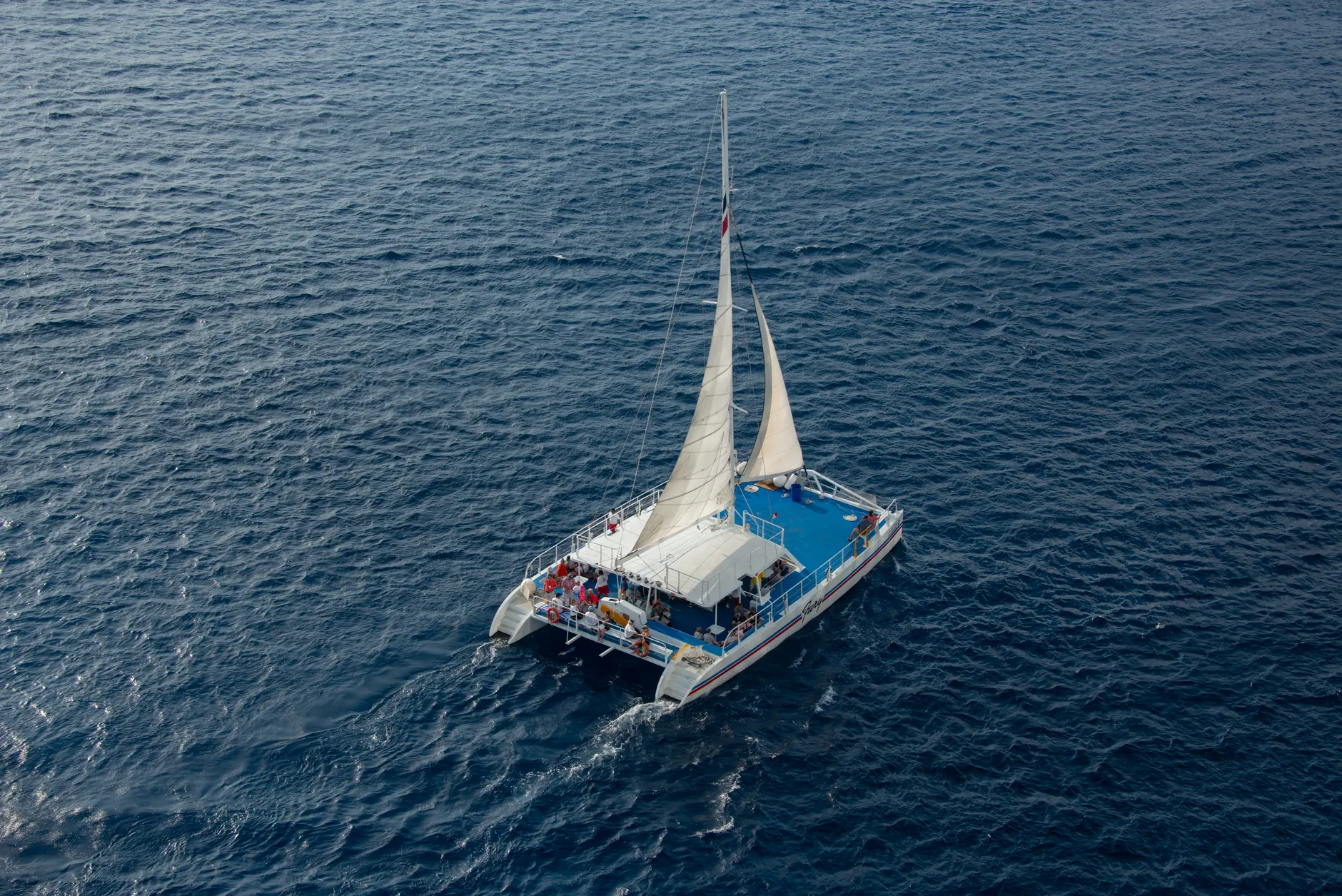 Aerial shot of a catamaran sailing with passengers on a clear blue sea.