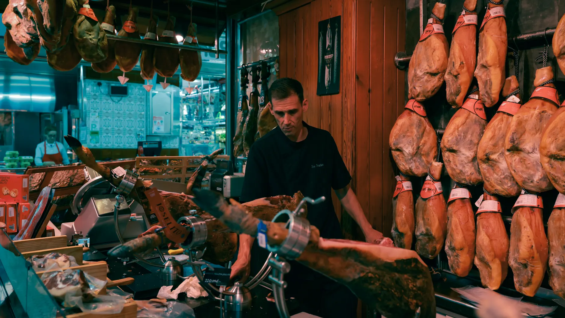 Man slicing Jamón in a traditional Barcelona market shop surrounded by hanging cured hams.