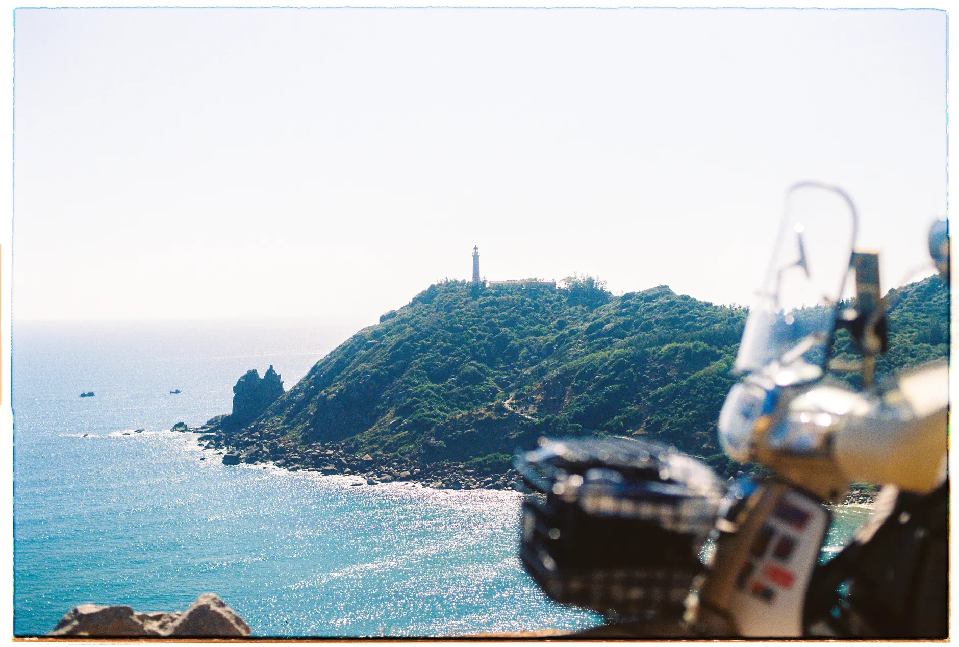 Scenic view of a lighthouse atop a hill by the coastline in Phú Yên, Vietnam with a motor scooter in the foreground.